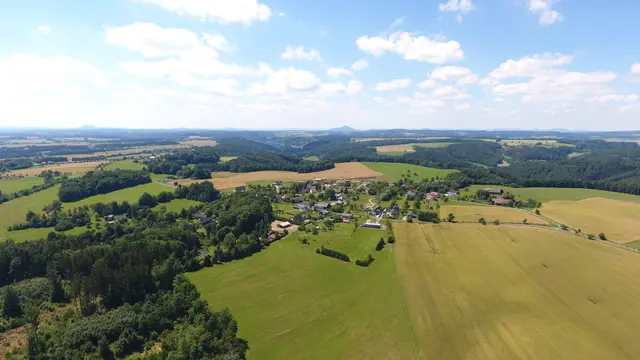 Pole a lesy kolem Jiviny, v dálce domy a kuželovitý kopec
