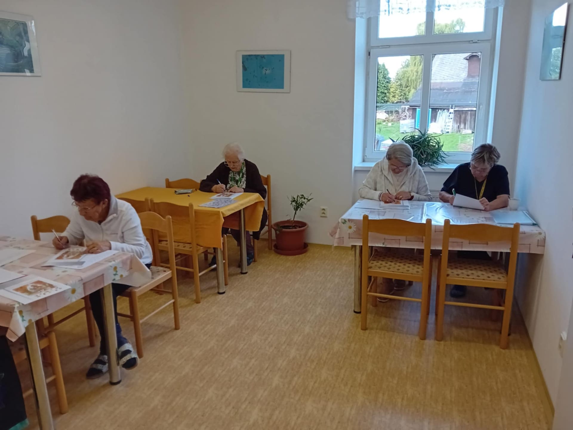 Čtyři ženy řeší úlohy u stolů v jídelně domu s pečovatelskou službou
