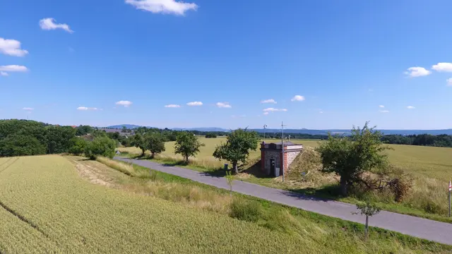 Silnice mezi poli s malou zděnou stavbou a stromy