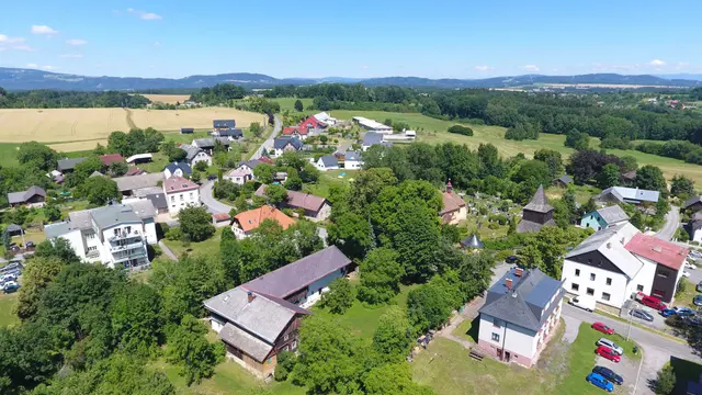 Střed Vlastibořic: dřevěná zvonice, bílé budovy a parkoviště s auty